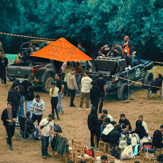 A tailgate party with trucks and people in a dirt parking lot.