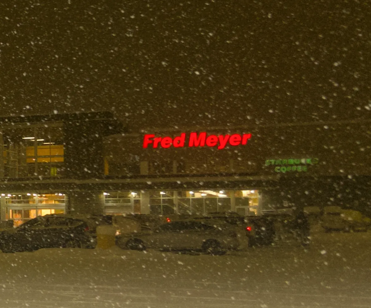 A glowing red Fred Meyer sign with snow falling in the foreground.