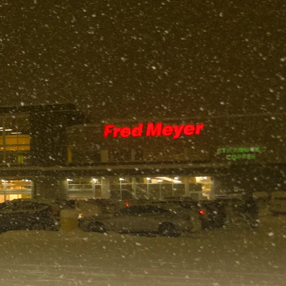 A glowing red Fred Meyer sign with snow falling in the foreground.