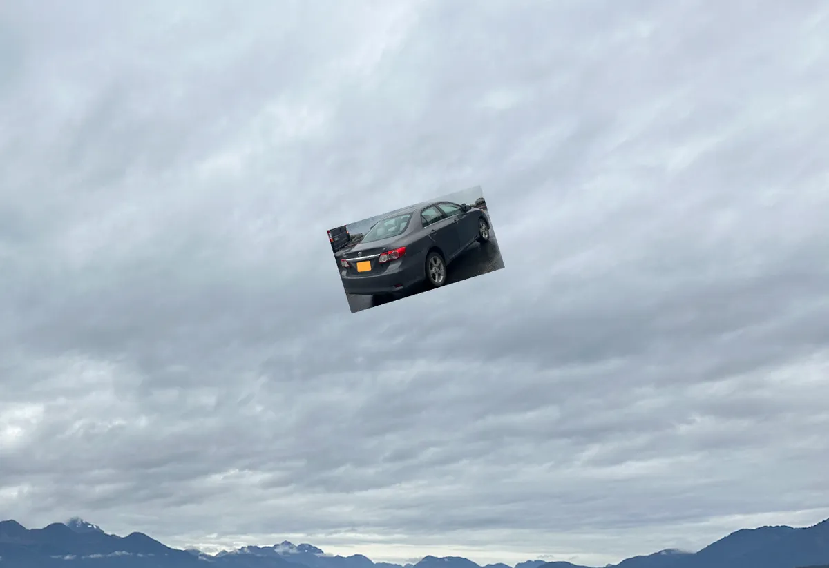 A small gray car flying in the clouds above faraway mountains. 
