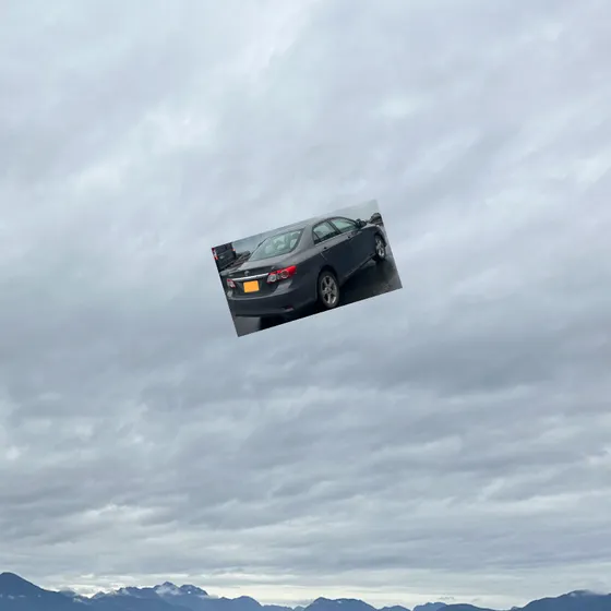 A small gray car flying in the clouds above faraway mountains. 
